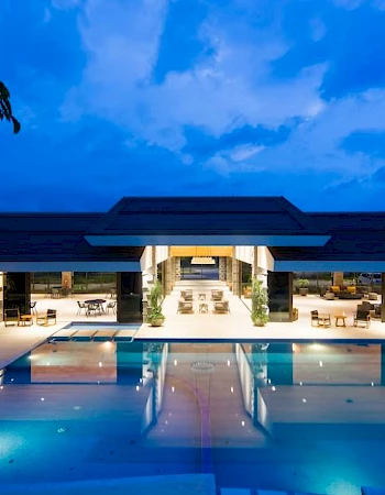 A luxurious outdoor pool area at night with a large illuminated building in the background and lounge areas surrounding the pool.
