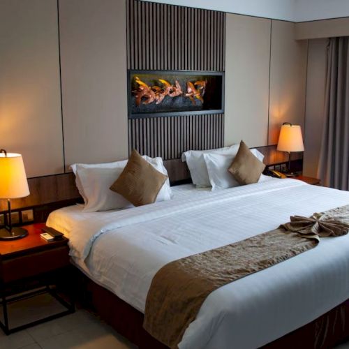 This image shows a modern hotel room with a large bed, two nightstands, lamps, a decorative item on the bed, and a front window with curtains.