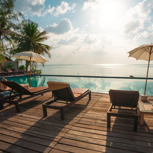 A serene beachside scene with lounge chairs, umbrellas, palm trees, and a tranquil ocean view at sunrise or sunset.