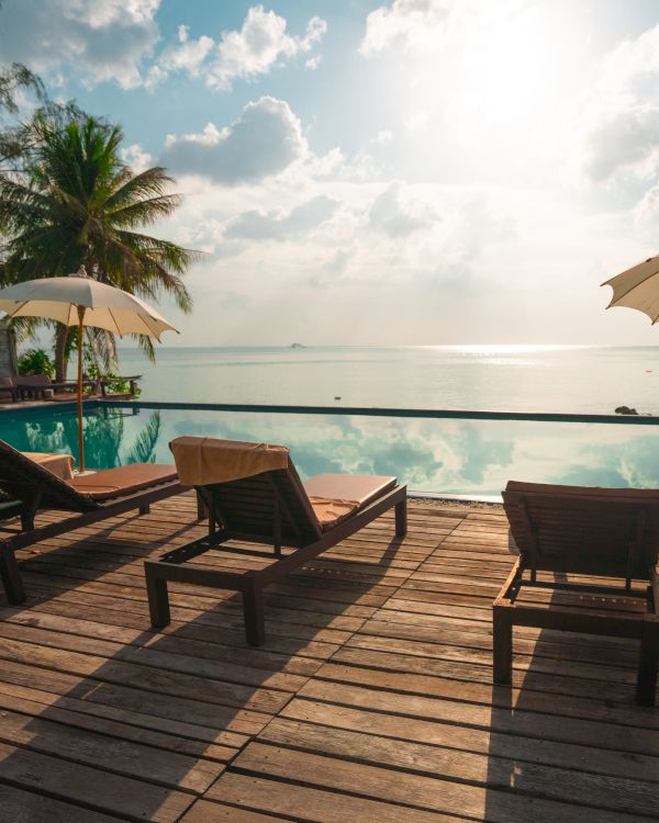 A serene beachside scene with lounge chairs, umbrellas, palm trees, and a tranquil ocean view at sunrise or sunset.