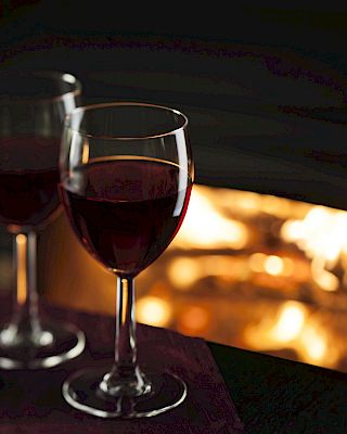 Two glasses of red wine sit on a table in front of a cozy fireplace, creating a warm and inviting atmosphere.