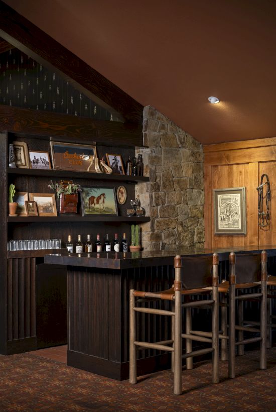 The image depicts a cozy home bar with wooden stools, shelves with various bottles, framed pictures, and rustic decor.