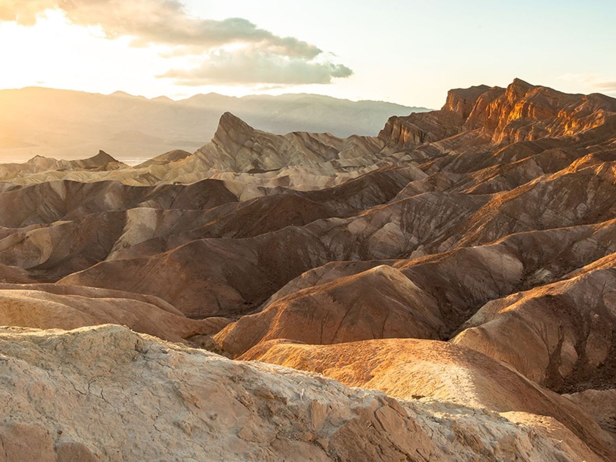 A sunset view of a desert landscape with rocky formations and mountains in the distance.