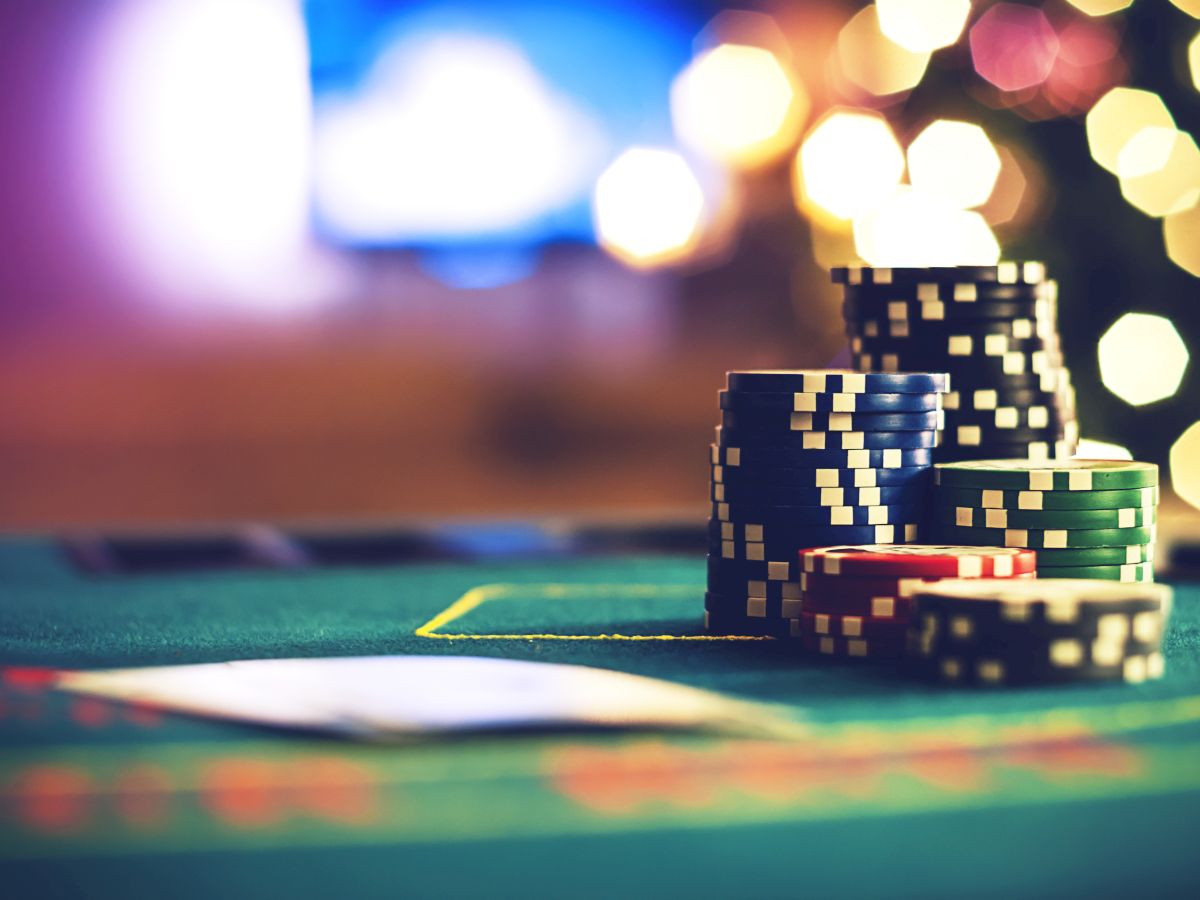 A stack of poker chips sits on a green casino table with blurred lights in the background, suggesting a lively atmosphere.