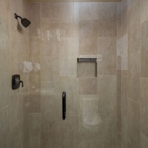 This image shows a tiled shower with a wall-mounted showerhead, faucet, built-in nook for toiletries, and a decorative handle on the wall.