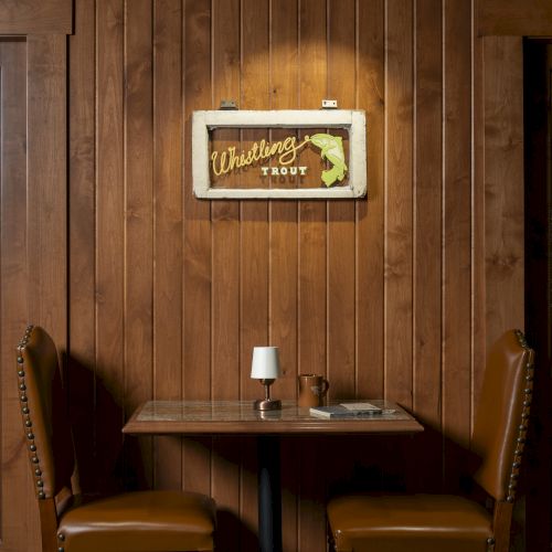 A small dining table with two chairs against a wooden wall, featuring a dim light and a decorative 