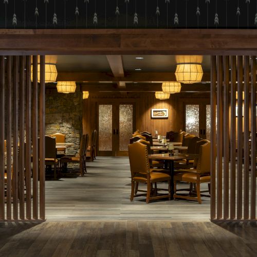 The image shows the entrance to a cozy, dimly lit restaurant with wooden decor, featuring several tables and chairs arranged in a welcoming manner.