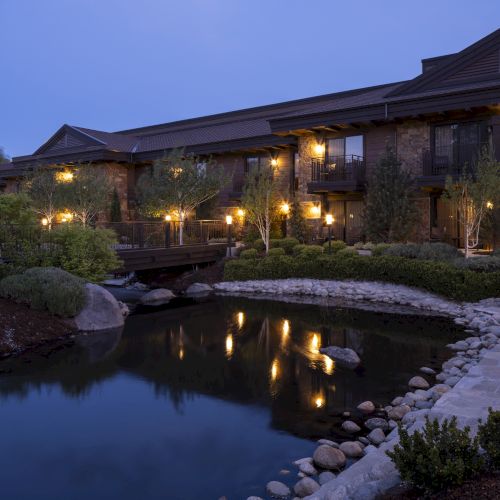 A serene evening scene of a hotel or resort with warm lights, a pond, and manicured landscaping, creating a peaceful atmosphere.