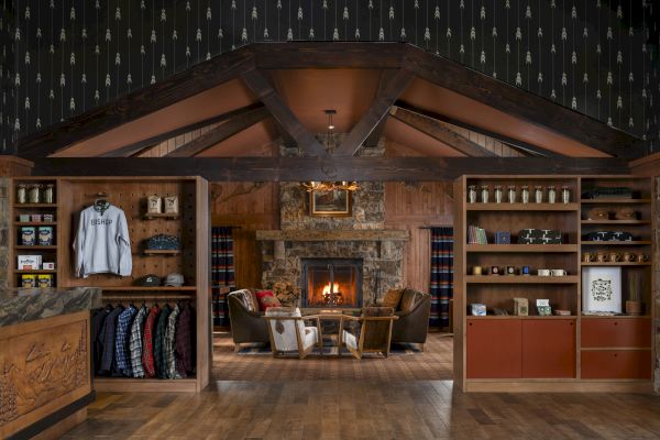 A cozy room with a fireplace, seating area, and wooden shelves displaying clothes and items, set in a rustic, lodge-like interior.