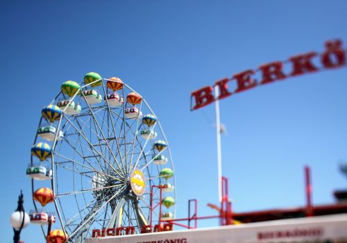 The image shows a vibrant Ferris wheel with colorful cabins, set against a clear blue sky. A 