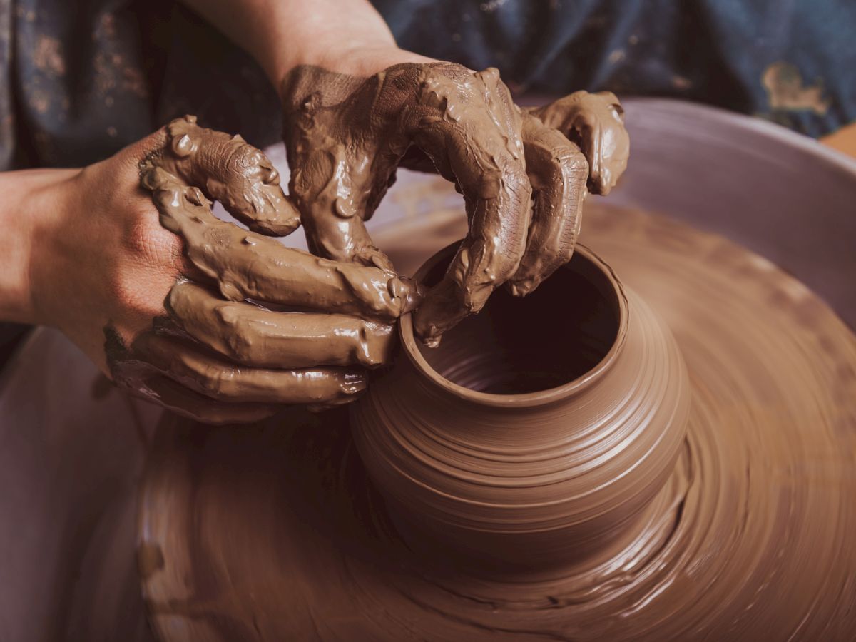 A person shaping a clay pot on a pottery wheel, hands covered in wet clay as the pot takes form.