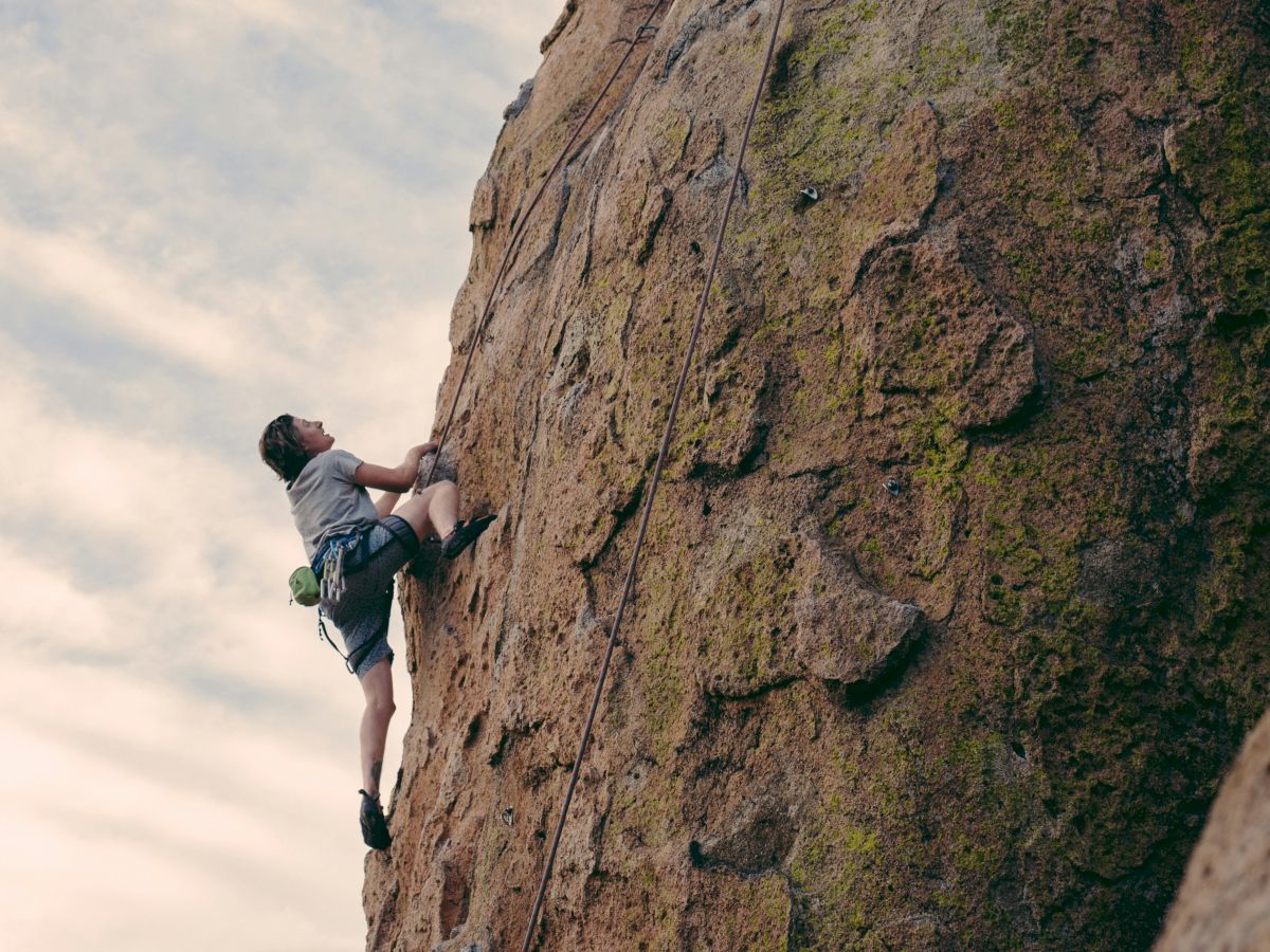 A person is rock climbing on a steep, rugged cliff face against a cloudy sky, using ropes and harnesses for safety and protection against falls.