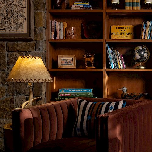 A cozy room with a wooden bookshelf filled with books and decor, a globe, framed artwork, a lamp, and a comfortable, striped couch.