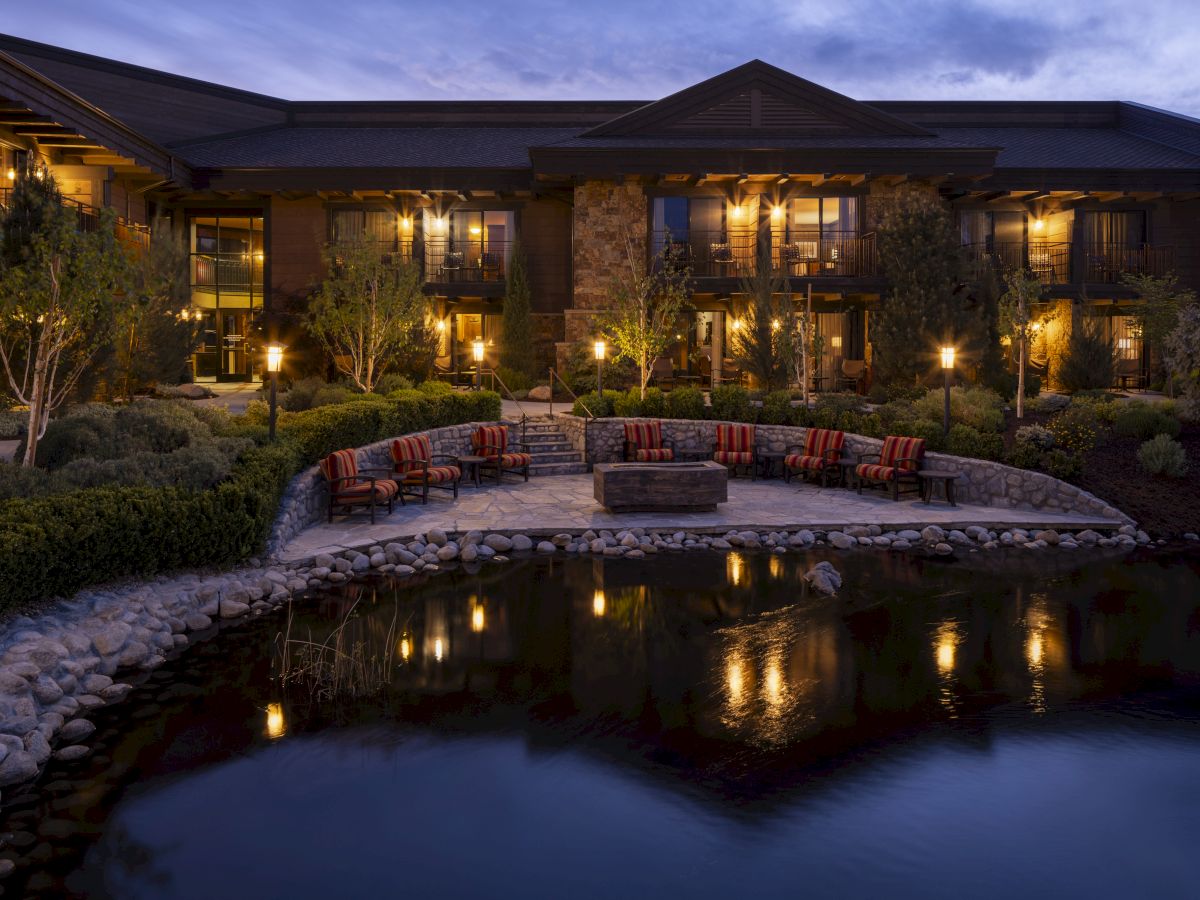 A luxurious lakeside villa with a lit patio, elegant seating around a circular water feature, reflecting warm lights at dusk. End.