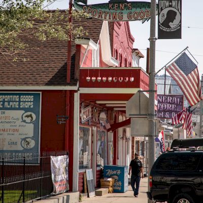 A street scene with a red building, several storefronts, American flags, and a person walking on the sidewalk.