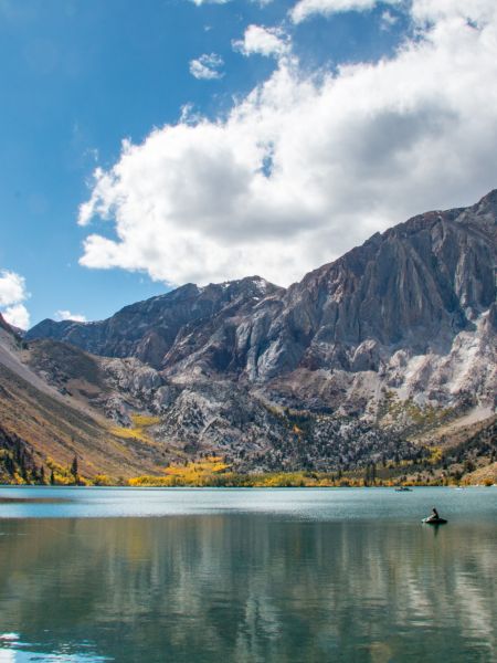 A serene lake with two kayakers is surrounded by rocky mountains under a partly cloudy blue sky.