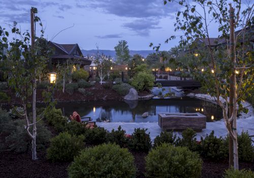 A serene outdoor landscape with trees, a pond, and a bridge, illuminated by soft lighting in the early evening.