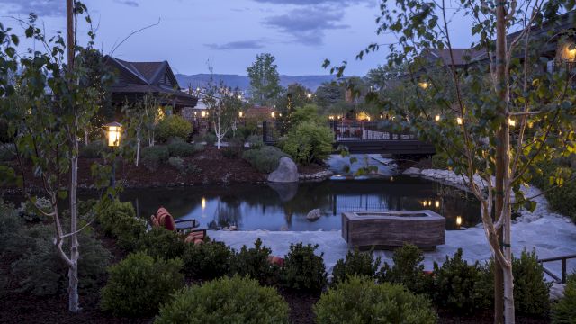 A serene outdoor landscape with trees, a pond, and a bridge, illuminated by soft lighting in the early evening.