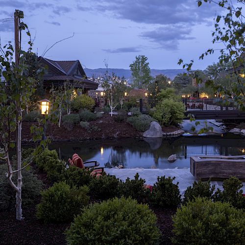 A serene outdoor landscape with trees, a pond, and a bridge, illuminated by soft lighting in the early evening.