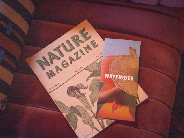 The image shows a "Nature Magazine" and a "Wayfinder" booklet on a maroon seat.