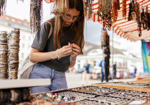 A person is browsing jewelry at an outdoor market stall, surrounded by various colorful bracelets and necklaces.