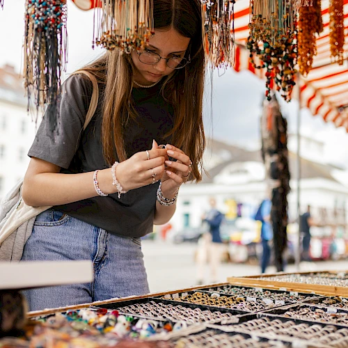 A person is browsing jewelry at an outdoor market stall, surrounded by various colorful bracelets and necklaces.