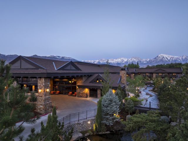 A large, rustic building surrounded by trees and mountains in the background, with soft lighting enhancing the serene atmosphere.