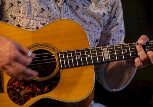 A close-up of a person strumming an acoustic guitar, fingers on the fretboard, strings vibrating as chords are played. Equal parts music and focus.