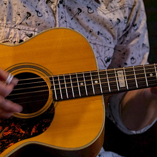 A close-up of a person strumming an acoustic guitar, fingers on the fretboard, strings vibrating as chords are played. Equal parts music and focus.