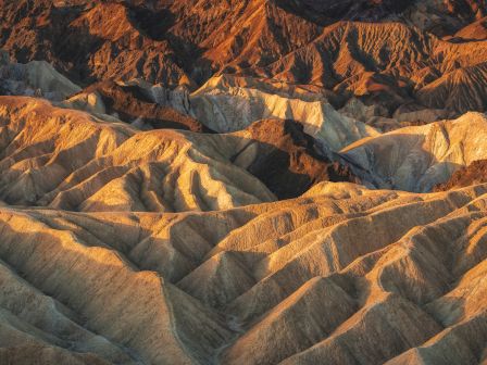 Rugged, wavy desert hills bathed in warm orange light, highlighting ridges and shadows across stark, layered terrain.
