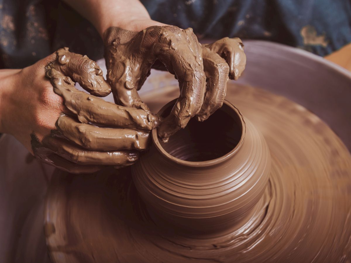 Hands shaping clay on a potter's wheel, smoothing a pot with muddy fingers, spinning pottery into a vessel as skill meets earth.