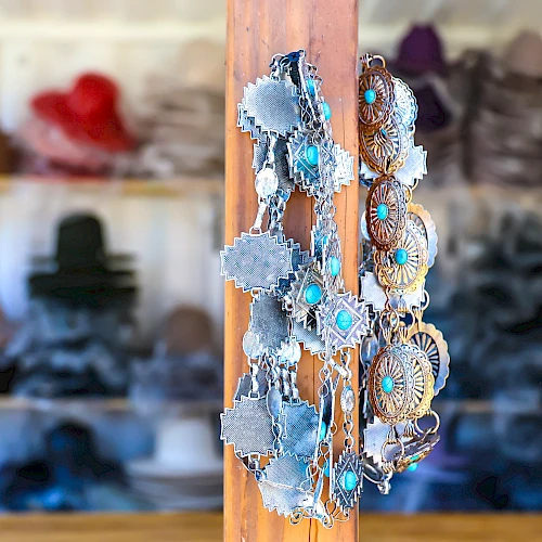 Shoe accessories hang on a wooden peg in a shop, with denim-fringed pieces and turquoise beads, while hats line the shelves in the background.