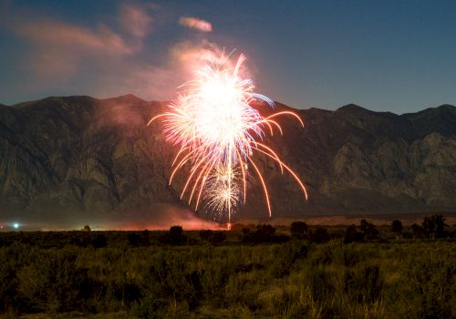 A bright fireworks display bursts over a dark valley with mountains in the background, sparks raining down into the night.