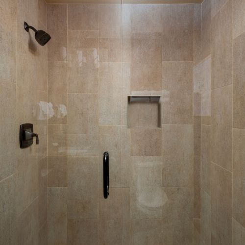 A tiled walk-in shower with a black showerhead, handheld fixture, and a recessed niche for toiletries.