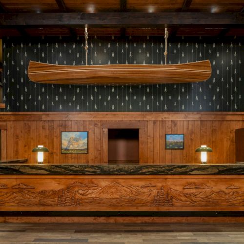 Rustic lodge bar with a carved wooden canoe-shaped display, wood paneling, pendant lights, and a marble counter.