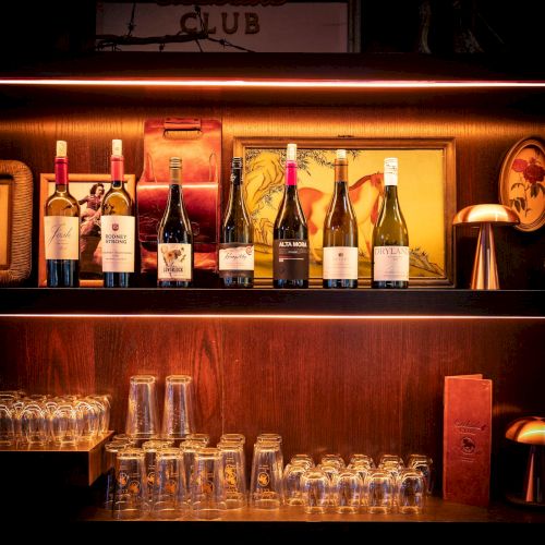 A bar display of wine bottles and glasses under warm light with a sign reading Geekside Club.
