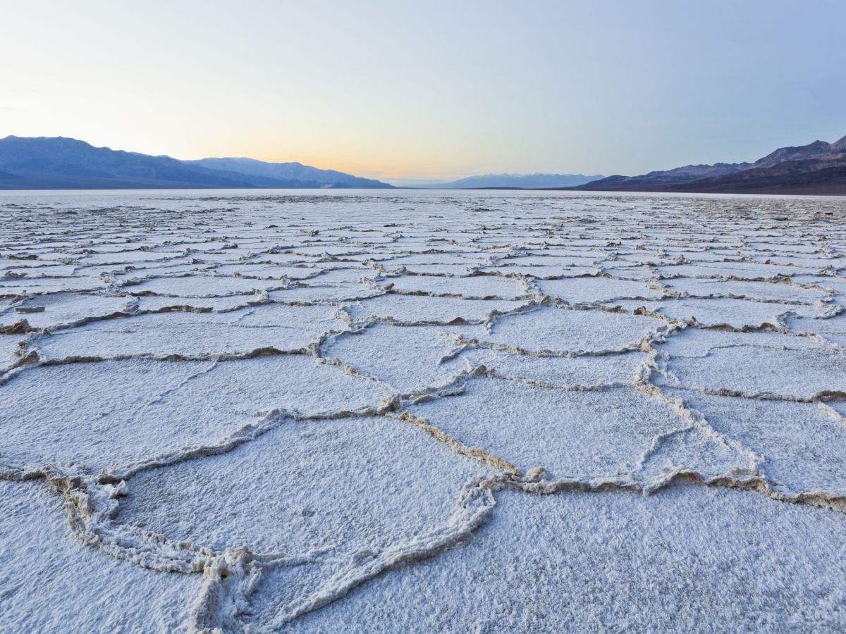 A vast salt flat covered in an icy crust and cracks, stretching to dark mountains under a dawn sky.