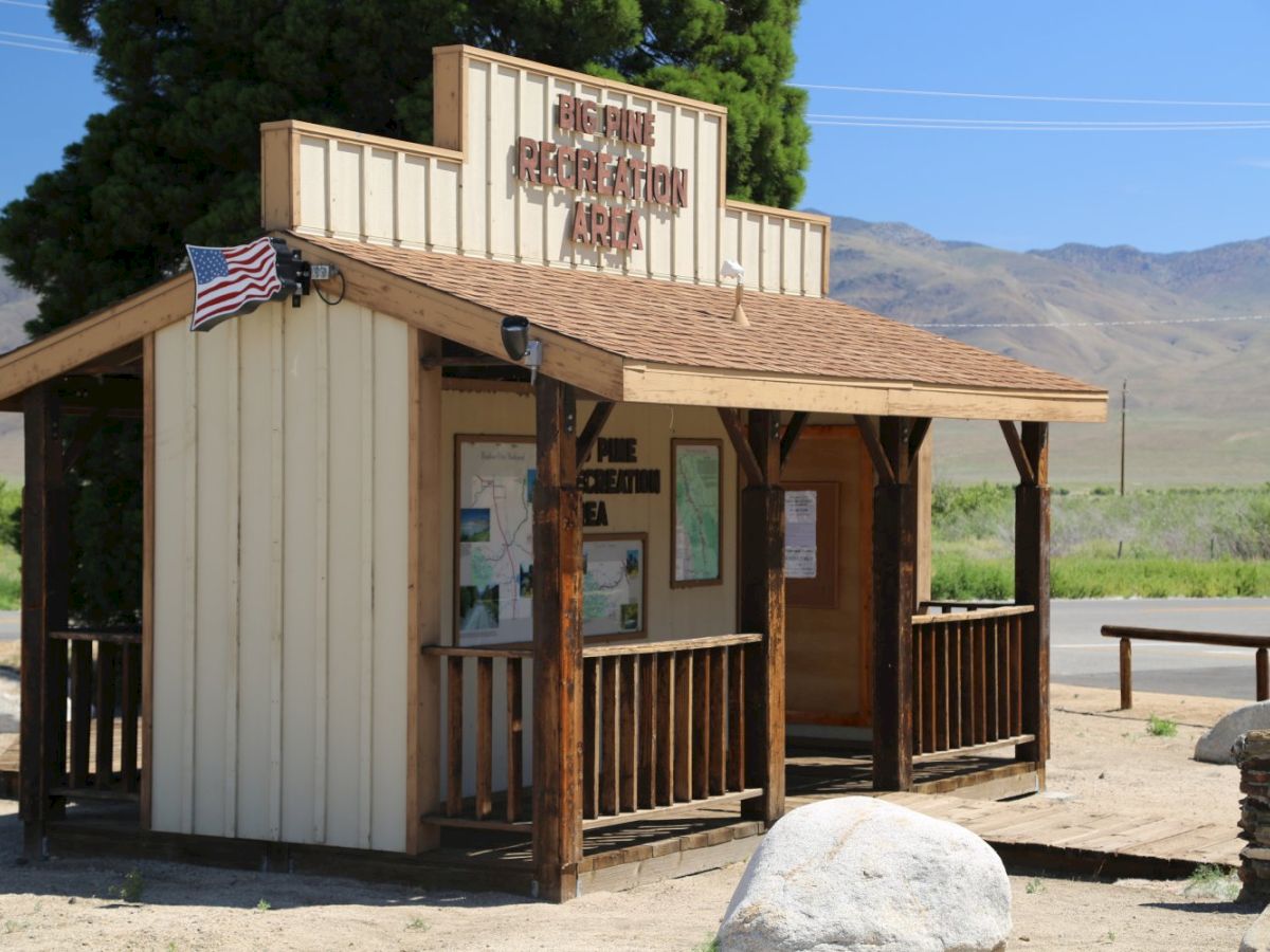 A &ldquo;Big Pine Recreation Area&rdquo; visitor kiosk with a US flag, maps inside, and mountains in the background.