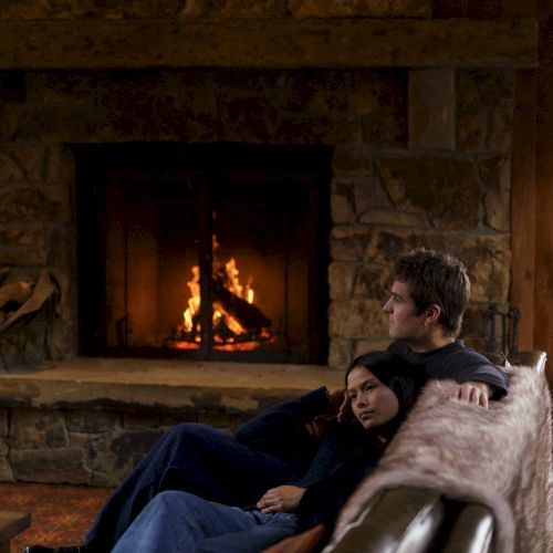 A cozy living room with a roaring fireplace as a man and child relax on a sofa under a blanket.