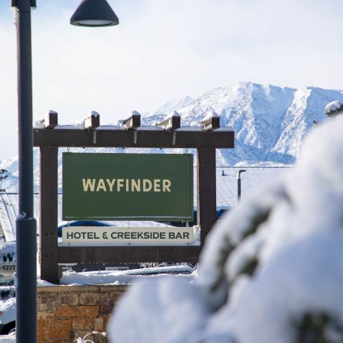Snowy mountain scene with a street sign reading WAYFINDER and Hotel & Creekside Bar, under a lamp post.