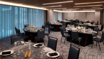 The image shows an elegantly set dining room with round tables, chairs, floral centerpieces, and folded napkins, creating a sophisticated ambiance.