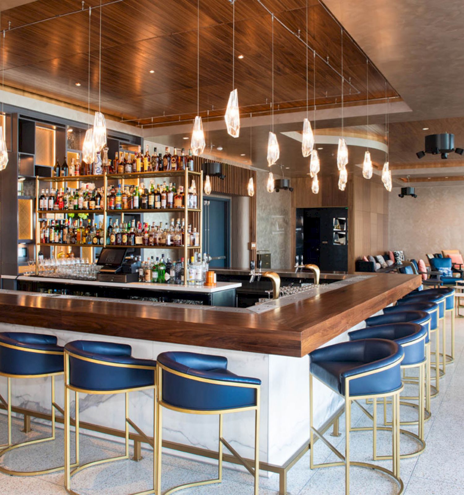 This image shows a modern bar with high stools, a stocked bar, and pendant lights, set in an upscale, spacious dining/lounge area.