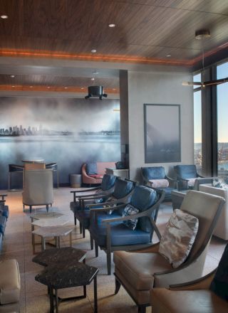 A modern, elegantly furnished lounge with numerous chairs, a large window offering a scenic view, and a wall mural depicting a cityscape.