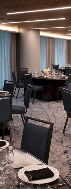 The image shows an elegant dining room set up for an event, with round tables, chairs, and table settings including glassware and napkins.