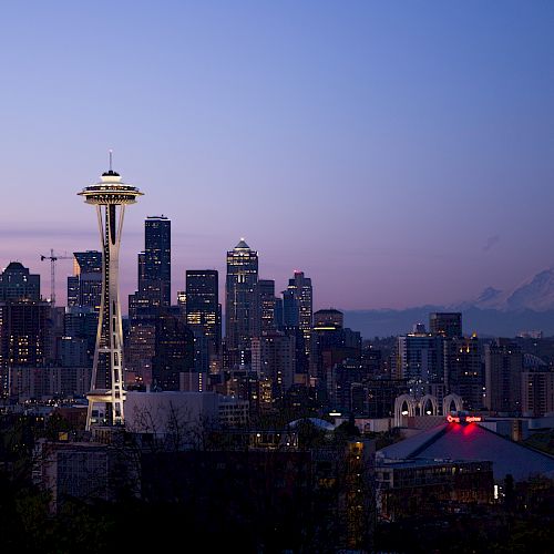 The image shows the Seattle skyline at dusk, featuring the Space Needle and skyscrapers with Mount Rainier visible in the background.