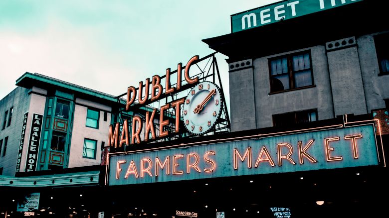 This image shows the entrance sign of a public market and farmers market, with the word "HOTEL" visible on a building in the background.