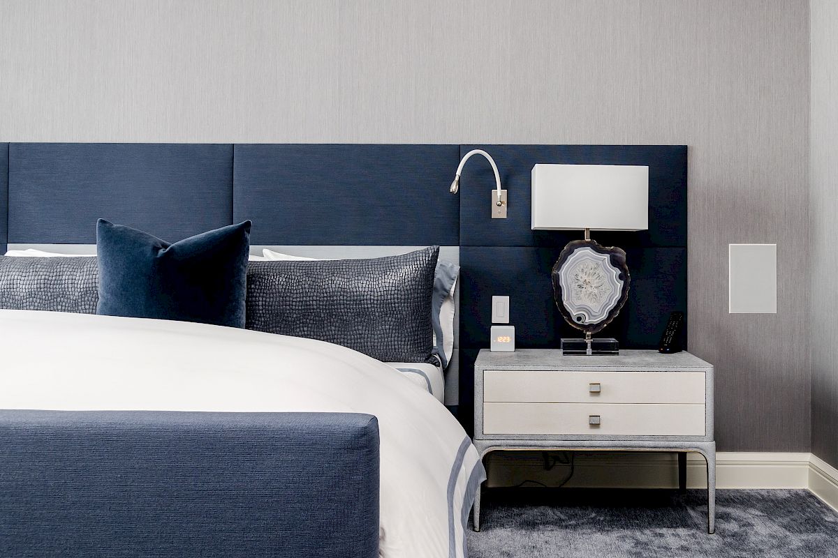 A modern bedroom with a navy blue and white color scheme, featuring a bed, nightstand with lamp, and decorative pillows, ending the sentence.
