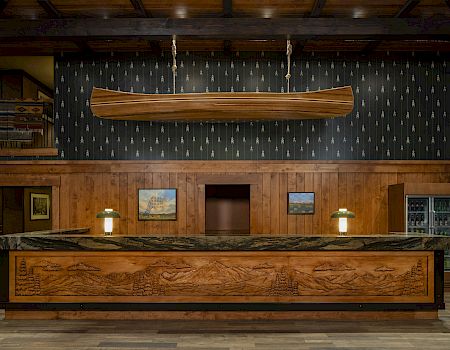 A warmly lit hotel lobby bar with a large carved wooden canoe/longboat centerpiece hanging from the ceiling.